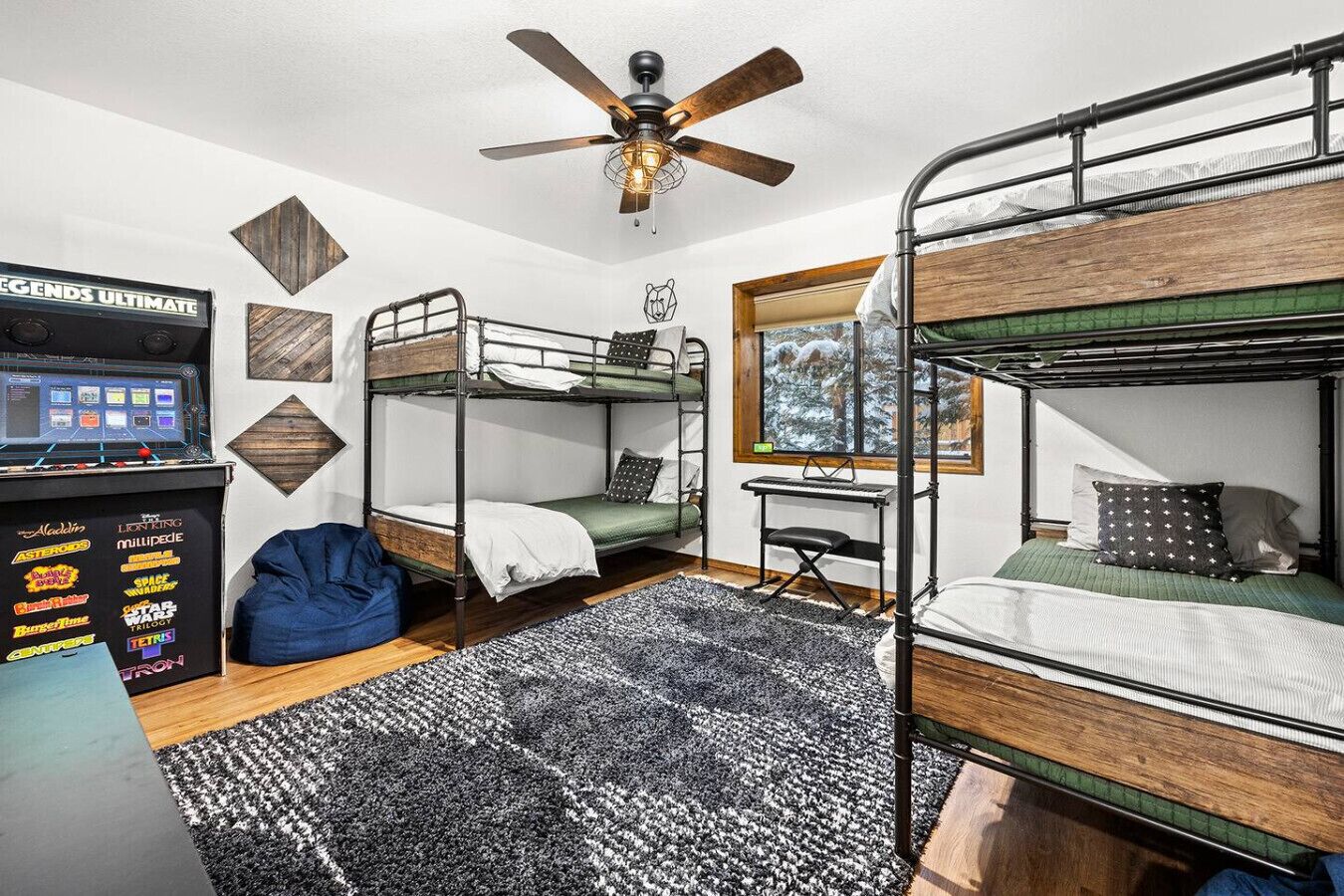 Een slaapkamer met stapelbed, een plafondventilator, een bureau met computer en een raam met uitzicht op sneeuw.