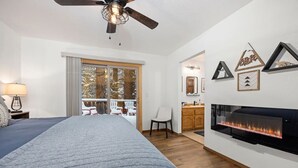 Een slaapkamer met een bed, een plafondventilator, een open haard en uitzicht op een besneeuwd terras.