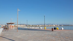A paved waterfront promenade with a bicycle, a covered seating area, and a row of colorful spherical sculptures.