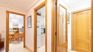 A hallway with wooden doors, a dining area with chairs and a table, and a kitchen visible through an open door.