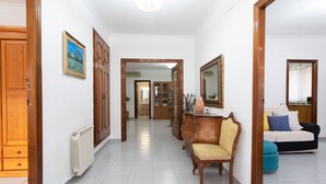 Un pasillo con puertas de madera, un radiador, una silla, un sofá y un espejo.