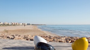 Una playa con un paseo marítimo pavimentado, un litoral rocoso y edificios al fondo.