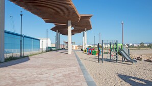 Un pasillo cubierto con un parque infantil, una cerca azul y un cielo despejado.