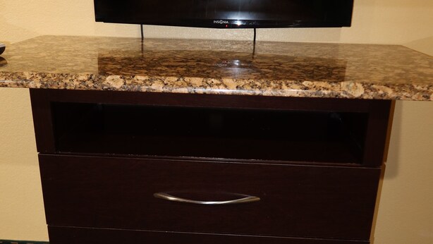 Un mueble de madera oscura con un televisor de pantalla plana encima, cajones y una alfombra estampada.