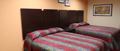 A hotel room with two beds, each with a patterned bedspread, a dark headboard, and a framed picture on the wall.