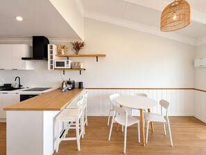 Una cucina moderna con mobili bianchi, un'isola in legno e un'area da pranzo con sedie bianche.