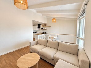 Un soggiorno moderno con un divano beige, un tavolino rotondo in legno e un'area pranzo con sedie bianche e un piccolo tavolo.