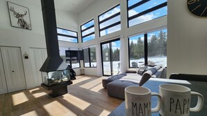 A modern living room with a fireplace, large windows, and a cozy seating area. - Ô paradis Spa&Massage (Weedon)