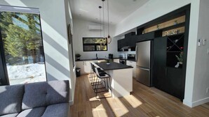 A modern kitchen with a large island, black cabinets, and stainless steel appliances. - Ô paradis Spa&Massage (Weedon)