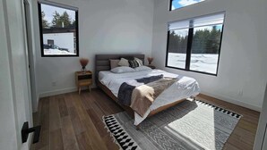 A bedroom with a bed, two bedside tables, a large window, and a view of a snowy landscape. - Ô paradis Spa&Massage (Weedon)