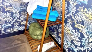A wooden rack with folded clothes and a green pillow against a patterned wallpaper background.