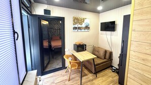 A compact living space with a bed, a sofa, a small table, a TV, and a microwave.