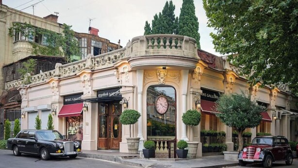 A building with a clock, a wine gallery, and two parked cars.