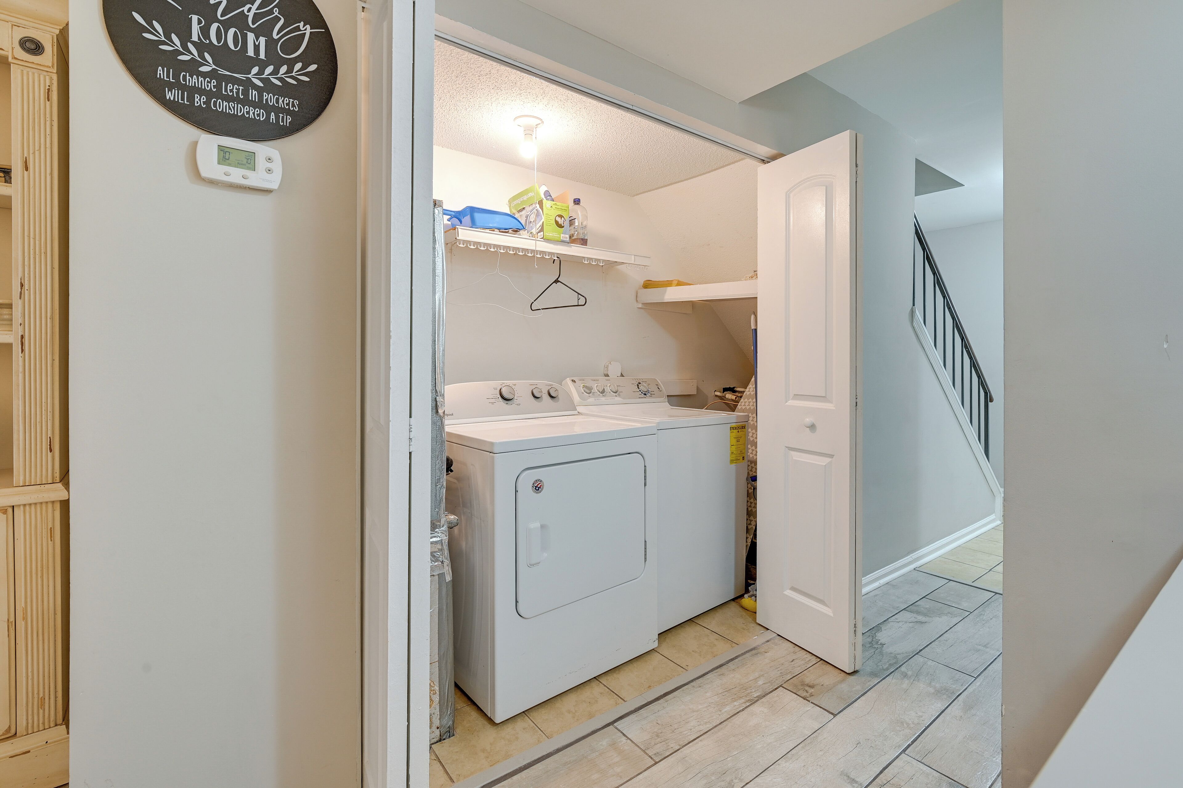 A laundry room with a washing machine and dryer, a small shelf with cleaning supplies, and a door leading to a staircase.