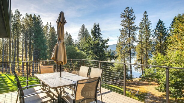 A deck with a table and chairs, overlooking a forest and a body of water. - Lake-View Apt w/ Furnished Deck in Hayden! (Hayden)