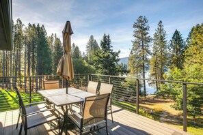 A deck with a table and chairs, overlooking a forest and a body of water. - Lake-View Apt w/ Furnished Deck in Hayden! (Hayden)