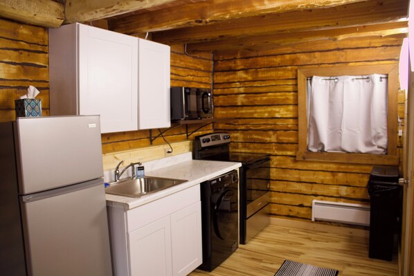 A compact kitchen with a refrigerator, microwave, oven, and dishwasher. - Petite Cabin With Ladder Loft (Wasilla)