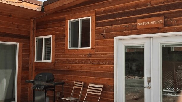 A wooden cabin with a deck, a grill, and two chairs. - Native Spirit Cabin at Base Camp (Dumont)
