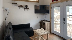A living room with a black sofa, a wooden coffee table, a flat-screen TV, and a sliding glass door leading to an outdoor area. - Native Spirit Cabin at Base Camp (Dumont)