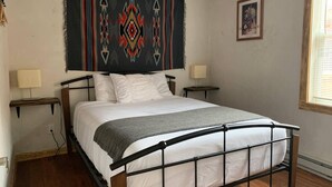 A bed with a metal frame, two bedside tables with lamps, a wall tapestry, and a framed picture. - Native Spirit Cabin at Base Camp (Dumont)