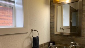 A bathroom with a glass bowl sink, a towel ring, a mirror, and a window with blinds. - Native Spirit Cabin at Base Camp (Dumont)