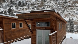Une cabane en bois avec une porte d’entrée en verre, située devant un paysage montagneux enneigé.
