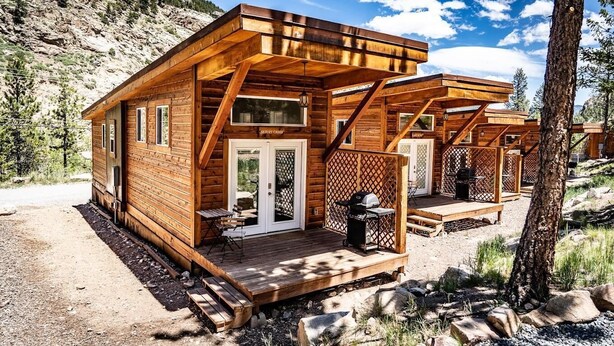 Une cabane en bois avec un porche, un barbecue et une pancarte sur laquelle on peut lire : « CAMP DE SKI ».