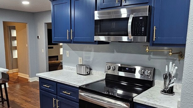 A modern kitchen with dark blue cabinets, stainless steel appliances, and a marble countertop.