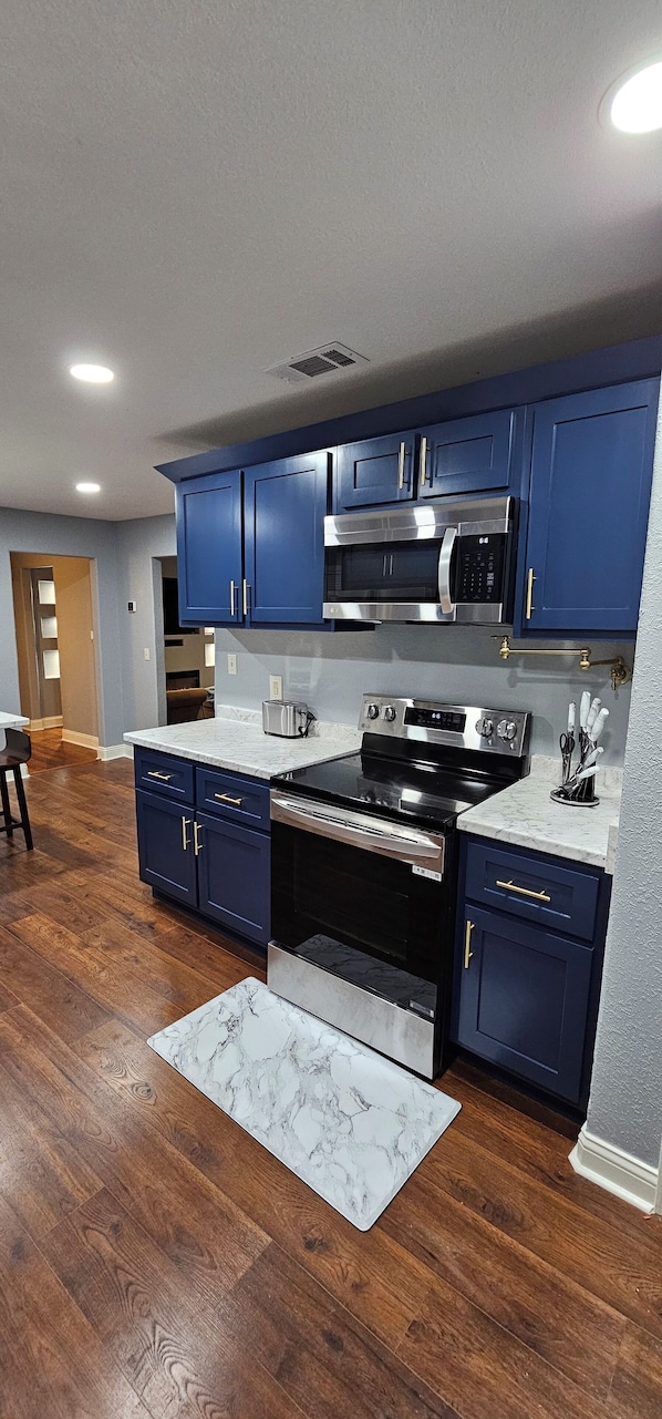 A modern kitchen with dark blue cabinets, stainless steel appliances, and a marble countertop.