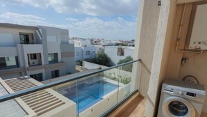 A modern apartment with a glass balcony overlooking a swimming pool and neighboring buildings.