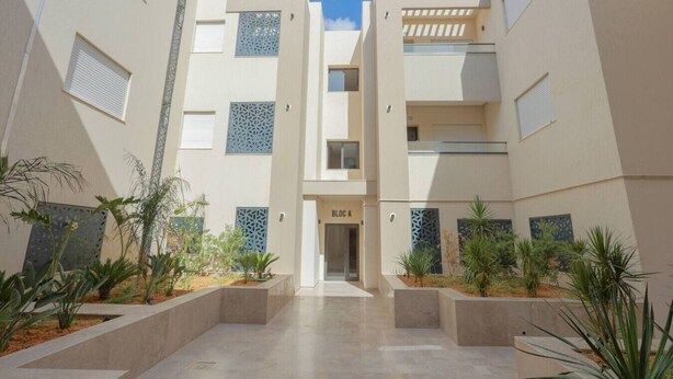 A modern building with a central entrance, multiple balconies, and decorative screens.