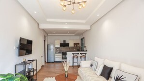 A modern living room with a sofa, coffee table, and TV. A kitchen is visible in the background.