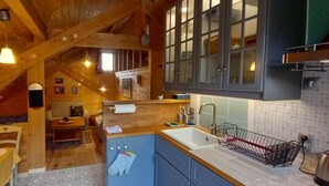 A cozy attic bedroom with a wooden ceiling, a small dining area, and a kitchen with blue cabinets and a white sink. - This mountain cocoon offers an idyllic setting for hiking enthusiasts. (Saint-Nizier-du-Moucherotte)