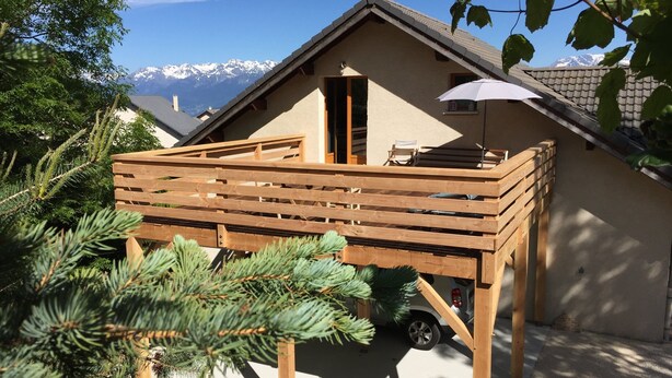 A chalet with a wooden deck, a car parked in front, and snow-capped mountains in the background. - This mountain cocoon offers an idyllic setting for hiking enthusiasts. (Saint-Nizier-du-Moucherotte)