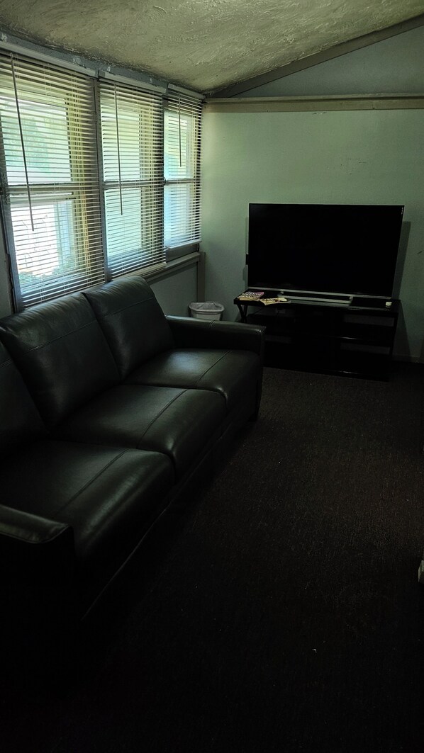 A living room with a black leather sofa, a flat-screen TV, and a small table with a remote control.