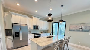 A modern kitchen with white cabinets, stainless steel appliances, a marble island, and a large window with a view. - Modern Retreat 3BR/2BA w/Pool in Rotonda West (Rotonda West)