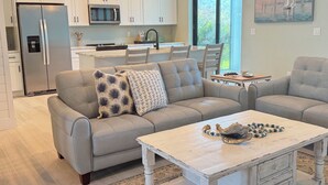A modern kitchen with white cabinets, a stainless steel refrigerator, and a microwave. There is a dining area with a table and chairs, and a painting on the wall. - Modern Retreat 3BR/2BA w/Pool in Rotonda West (Rotonda West)