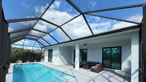 A modern indoor swimming pool with a glass ceiling, white walls, and a patio area with seating. - Modern Retreat 3BR/2BA w/Pool in Rotonda West (Rotonda West)
