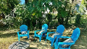 Un conjunto de cuatro sillas Adirondack azules con cojines estampados, dispuestas sobre un césped con un brasero cubierto cerca.