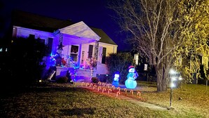 Una casa con porche decorado con luces navideñas y muñecos de nieve.