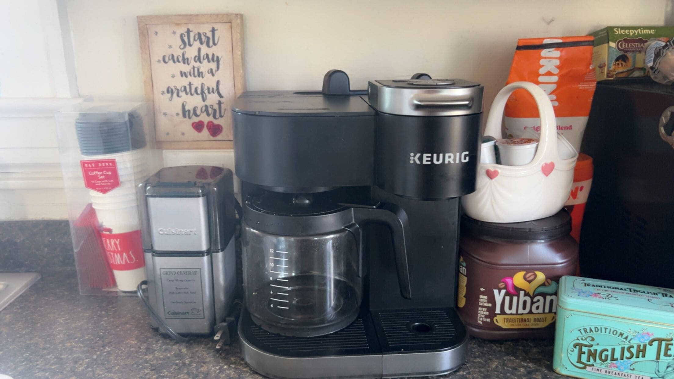 Una moka, una tazza di caffè, una mug, una scatola di tè e un cartello con una citazione.