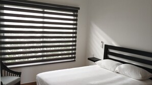 Une chambre à coucher avec un lit, une table de chevet, une chaise et une fenêtre avec des stores.