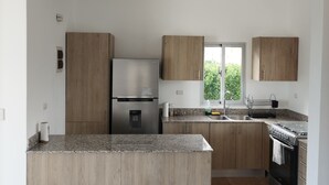 Une cuisine moderne dotée d’un îlot central, d’appareils électroménagers en acier inoxydable, de meubles en bois et d’une grande fenêtre qui laisse entrer la lumière naturelle.