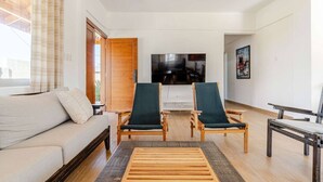 A modern living room with a sofa, two armchairs, a coffee table, and a TV.