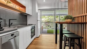 A modern kitchen with white cabinets, a black backsplash, and a wooden dining area with a bench and table. - Bright on the River Mystic Apartment 2 (Bright)