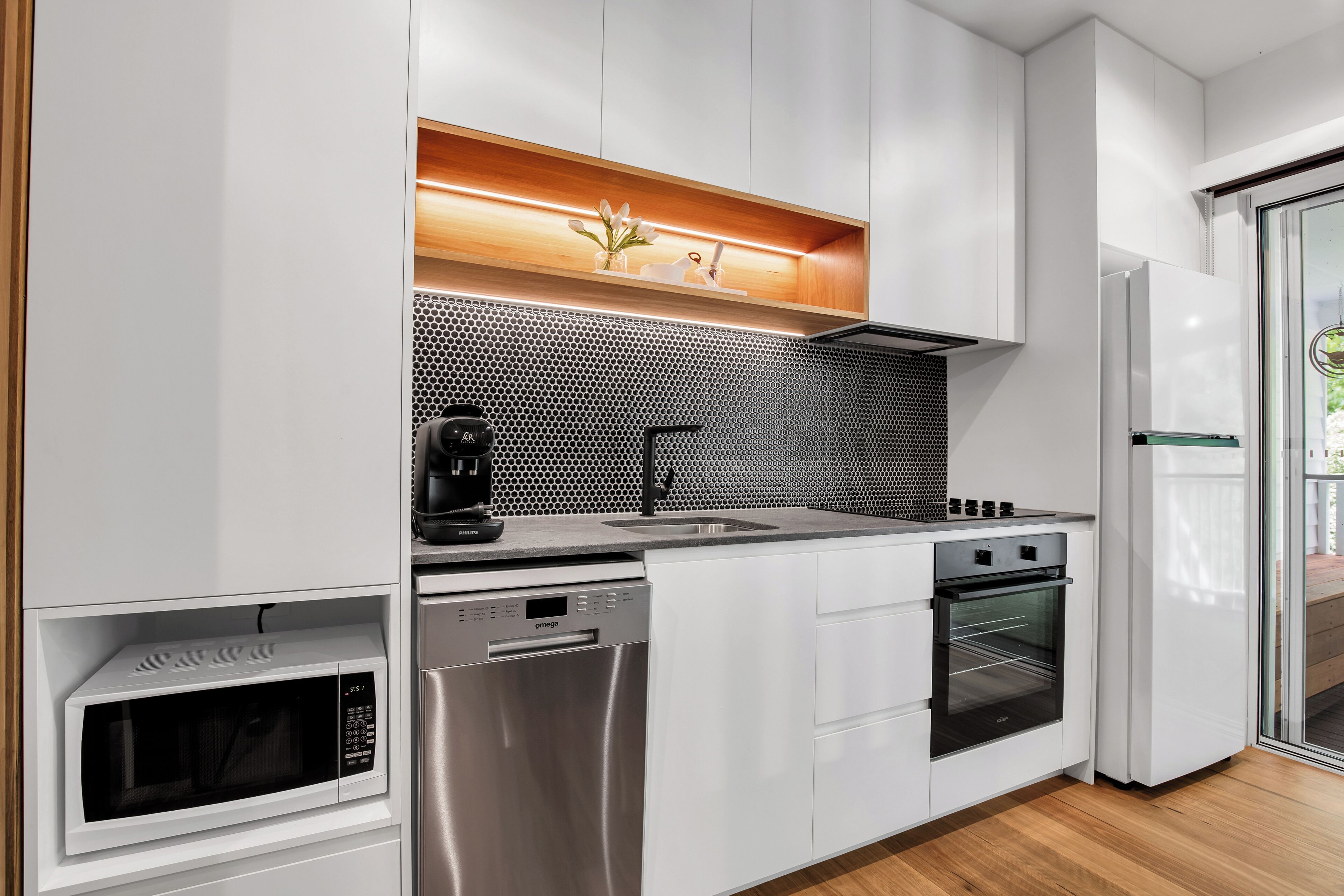 A modern kitchen with built-in appliances, a wooden shelf, and a glass door refrigerator.