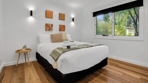 A modern bedroom with a large bed, a small bedside table, and a window with a view of trees. - Bright on the River Mystic Apartment 2 (Bright)