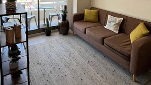 Una sala de estar con un sofá marrón, un tapete estampado y una ventana con persianas.