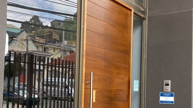 Una entrada de edificio moderna con una puerta de madera grande, paneles de vidrio y piso de baldosas.