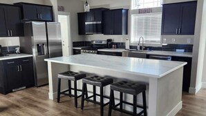 Una cocina moderna con armarios oscuros, electrodomésticos de acero inoxidable, una isla grande con taburetes de bar e iluminación colgante.